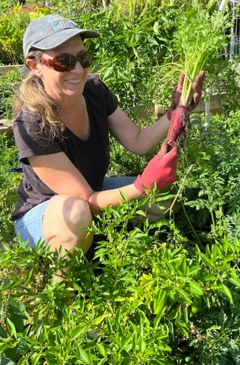 Melanie kneeling in the garden holding a freshly pulled bundle of carrots