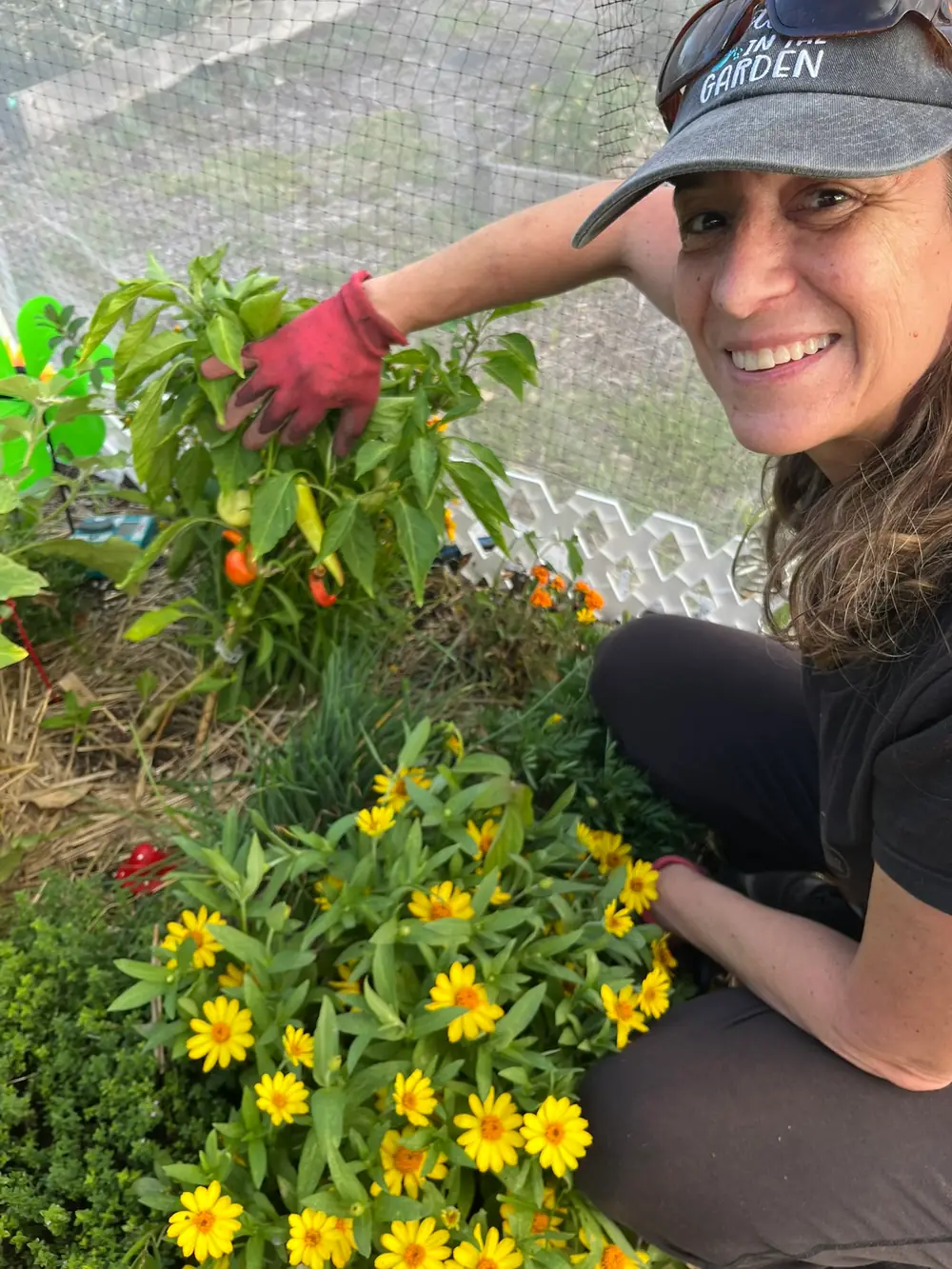 Melanie Kamburian kneeling among the vegetables and flowers in her South Florida community garden